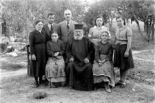Manolis Fatseas: Papa-Yakoumis and family. Standing, left, Manolis Tzannes (Flasketos) and his wife. To the right are their daughters Kreouza and Dinda. Seated either side of the priest are the paralytic (or partially paralysed) Lazaropoulos sisters. Standing in the centre is probably their...