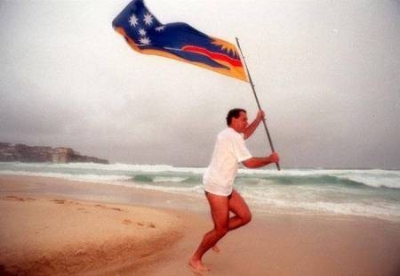 George C Poulos running across the sands of Bondi Beach with the official Bondi Beach Flag - his own design 