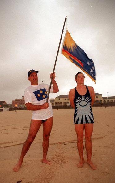 George C Poulos holding the official Rising Sun Flag of Bondi Beach over a life-saver wearing one of the original Bondi Beach Rising Sun Life Saver's uniforms from the 1920's and 1930's 